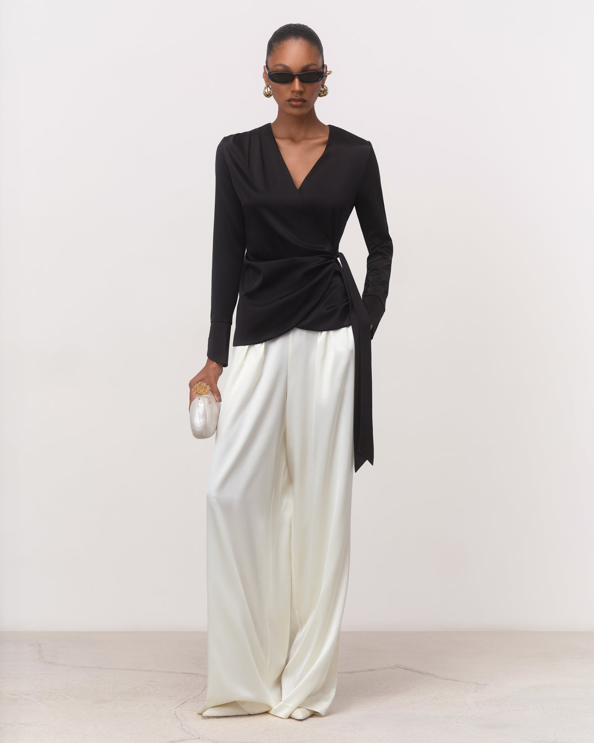 Anitas Muse Dubai black silk wrap blouse for women with V-neckline, worn with white wide-leg trousers, front view
