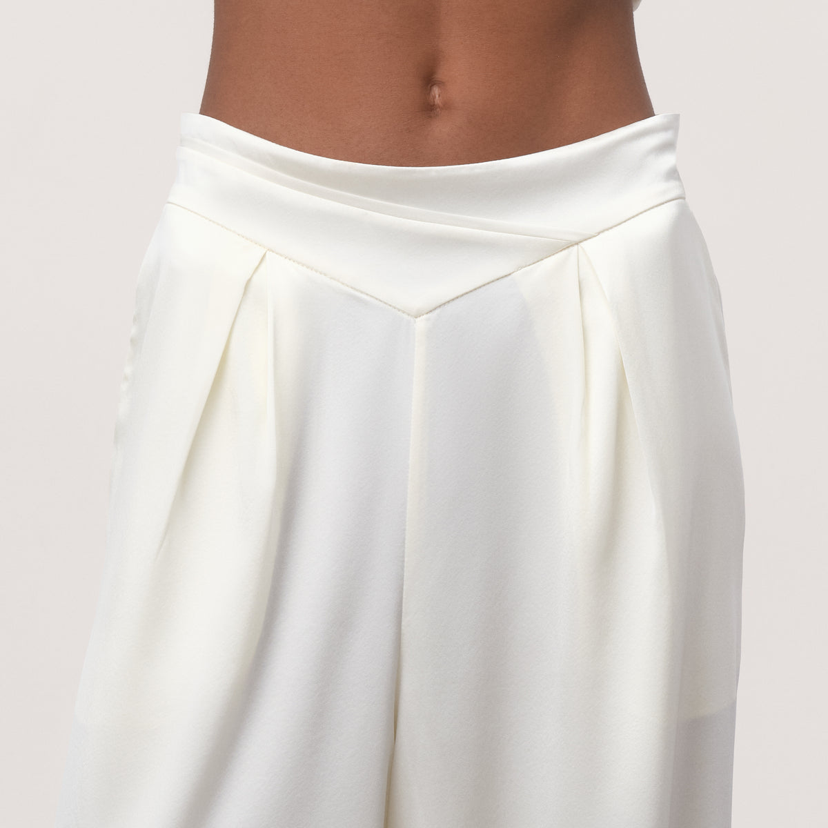 Close-up of white mulberry silk charmeuse wide-leg trousers with cross-front V-waistband and double front pleats
