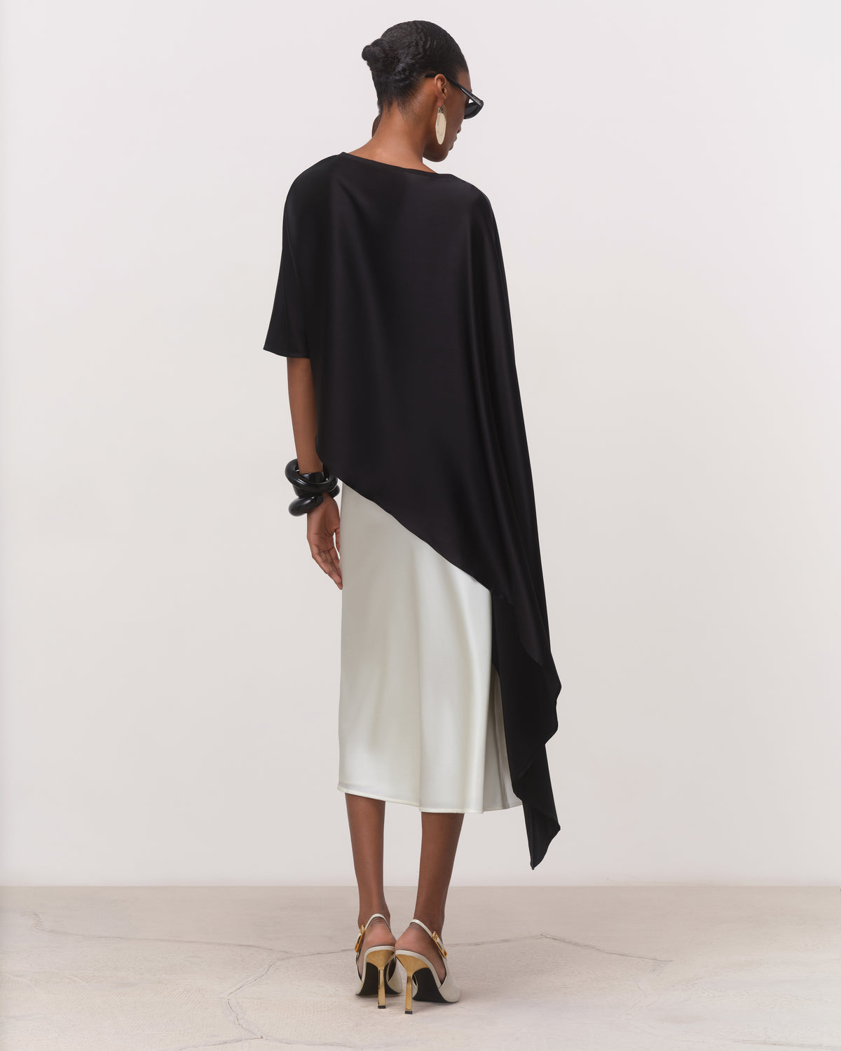 Back view of black boat neck silk cape top with draped hem