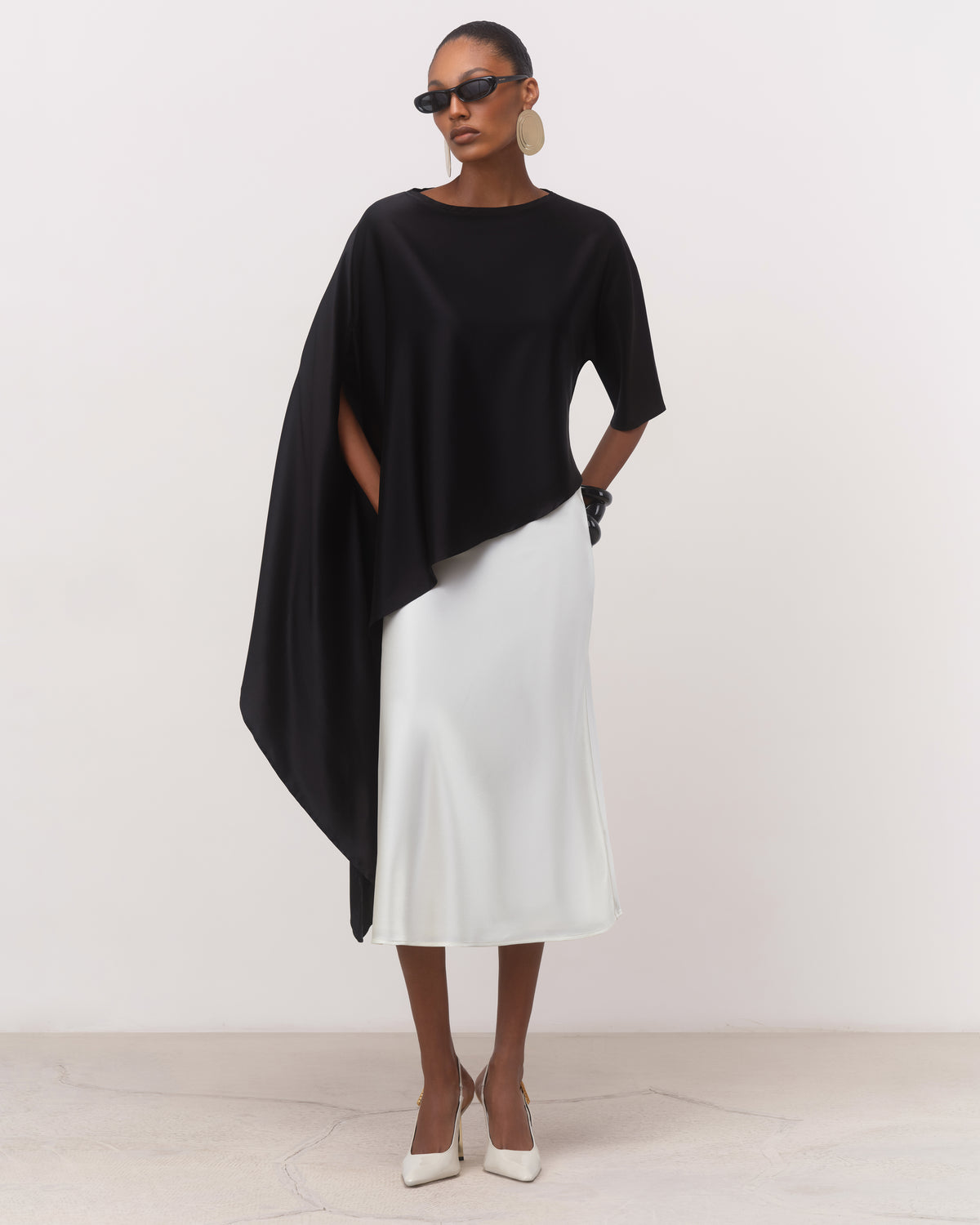 Women's black draped silk top with cape-like asymmetric hem, three-quarter view